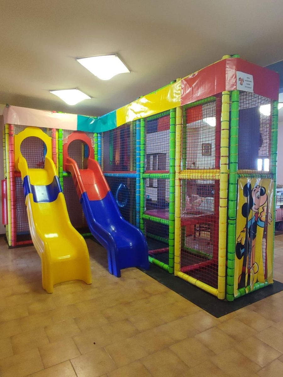Area bimbi con una struttura a castello colorata e due scivoli, dentro un locale